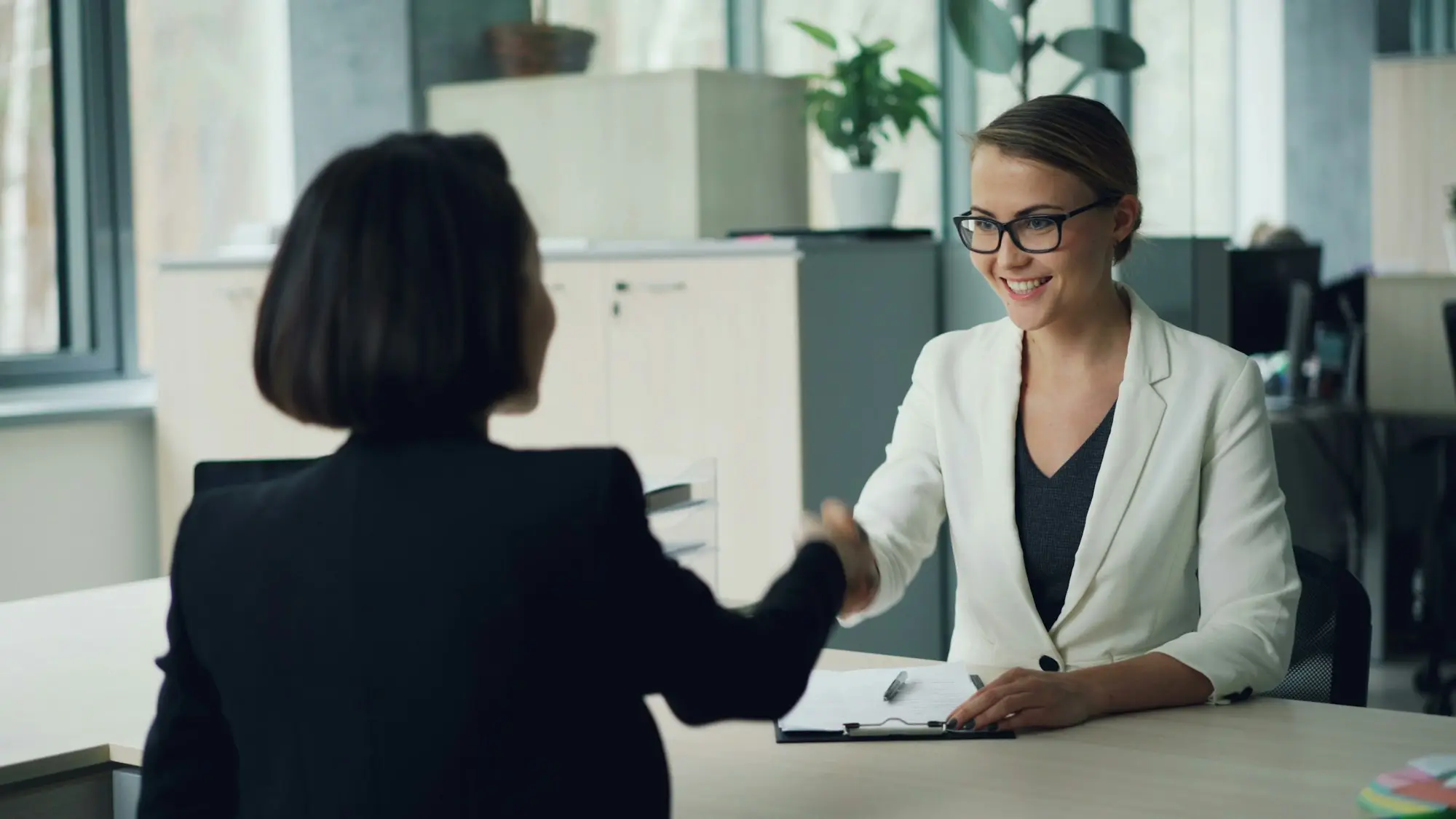 Two women shaking hands across a desk after a meeting